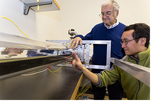 Professor Roland Winston (standing) and postdoctoral researcher Lun Jiang work on a solar collector system.